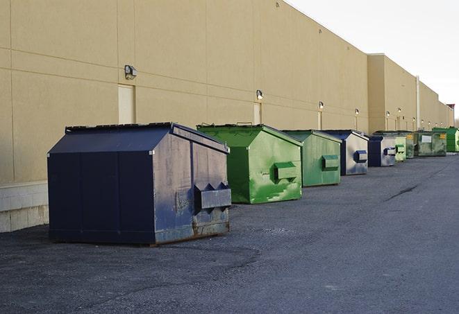 a construction worker unloading debris into a blue dumpster in Bristow